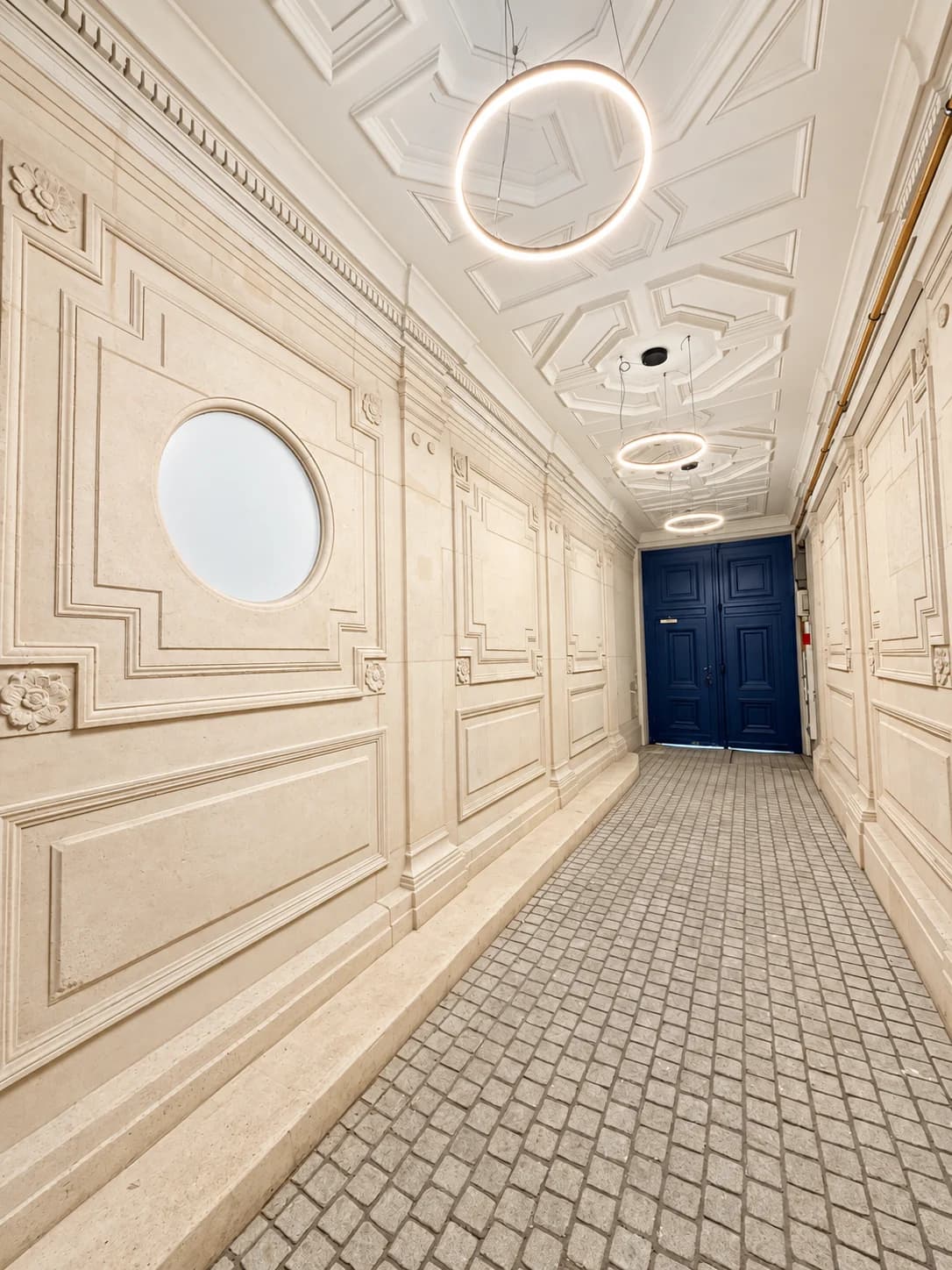 Hall d'entrée de l'immeuble haussmannien, murs en pierre moulurés et porte bleue