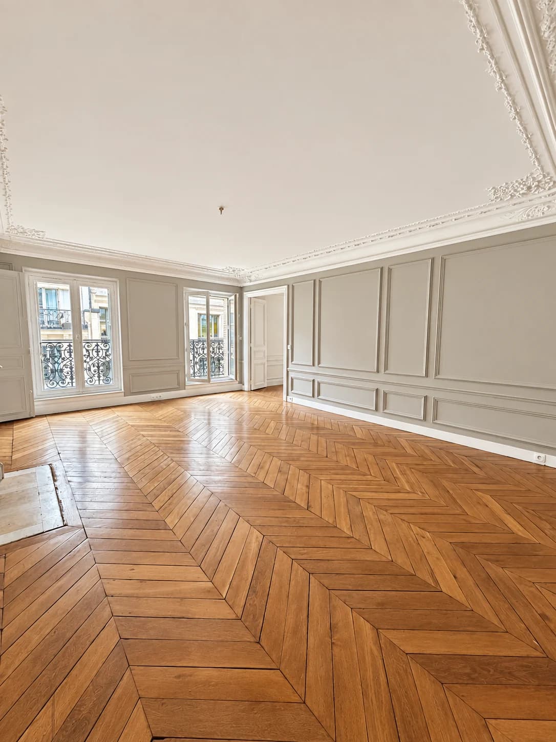 Salon vide, parquet en point de Hongrie et portes-fenêtres sur balcon